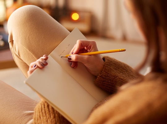A woman writes in a paper journal using a pencil.