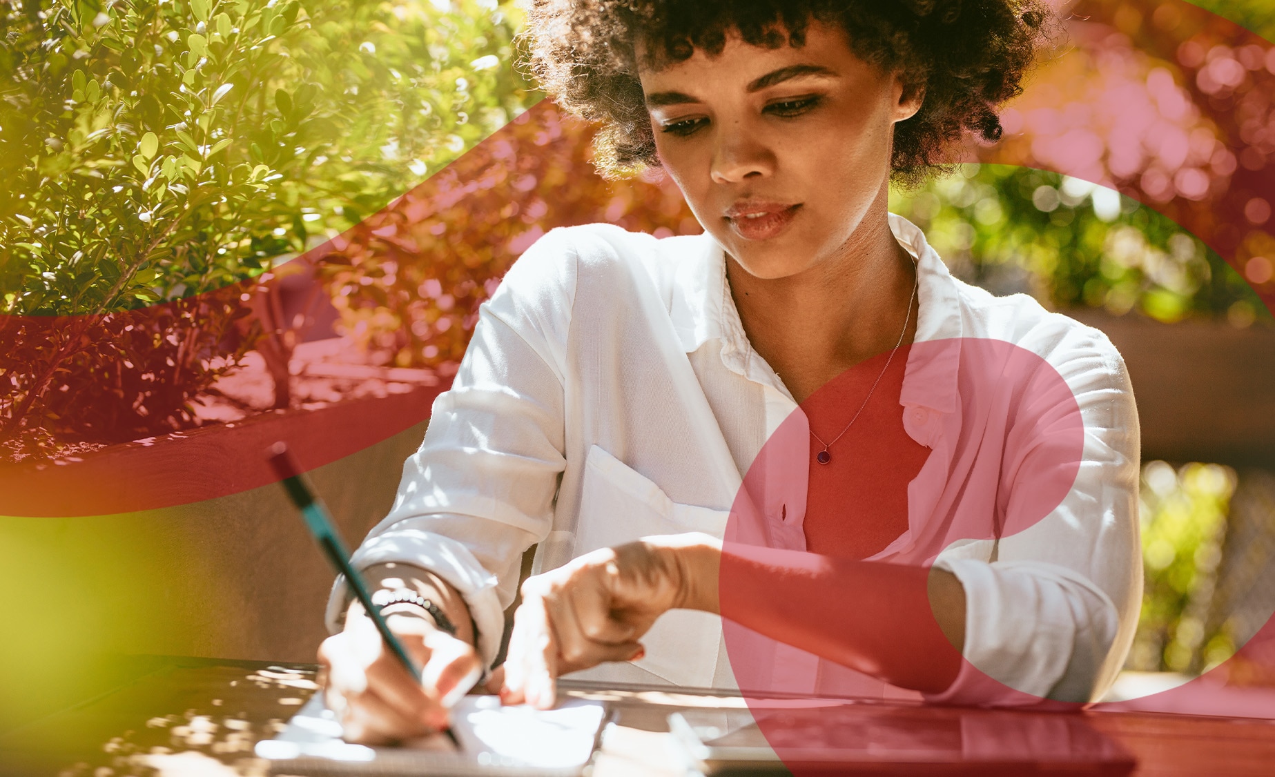 A woman sits at a garden table with a pencil writing in a notebook.