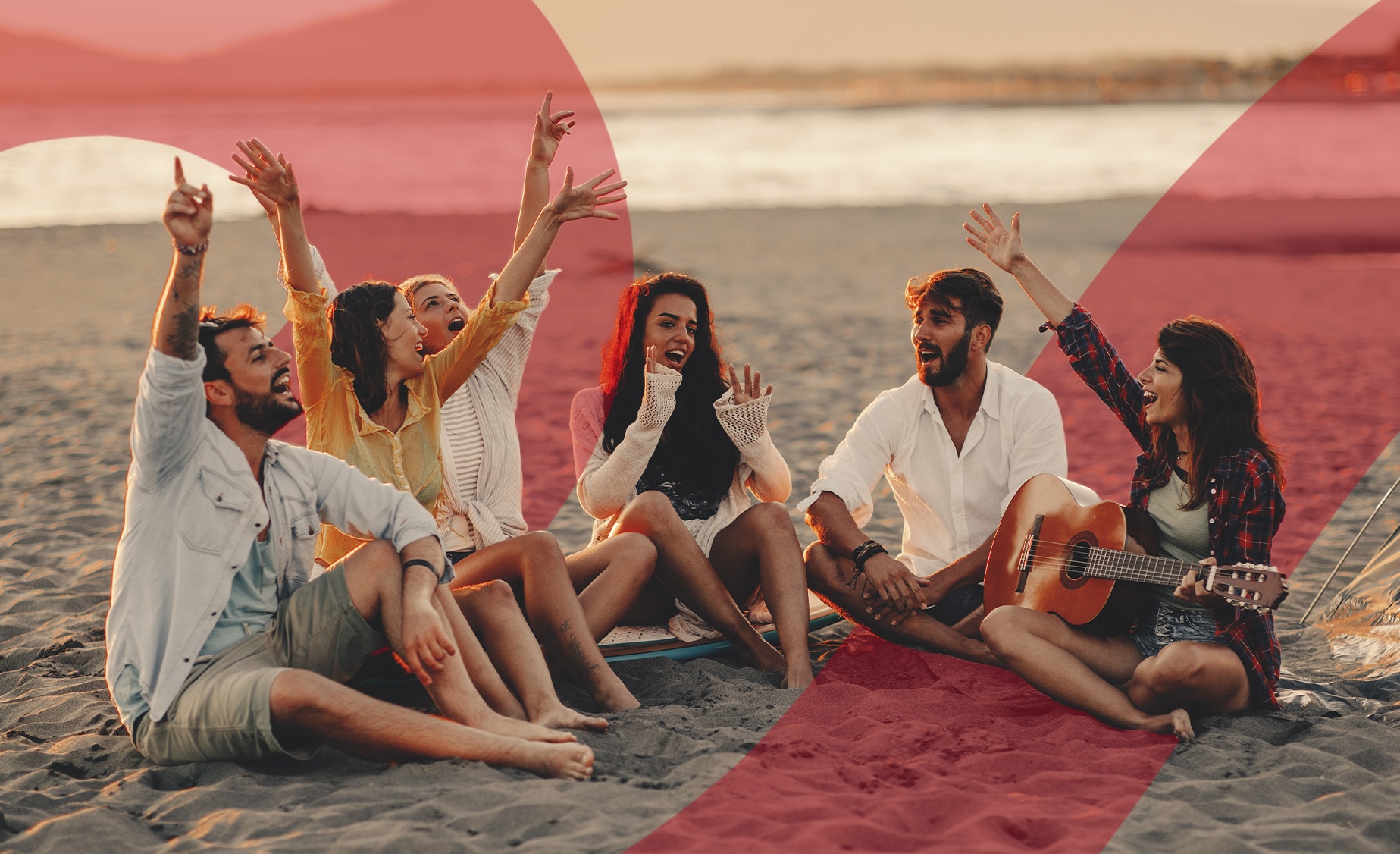  A group of people sitting on a sandy beach at sunset laughing and singing together while one of the women in the group plays
