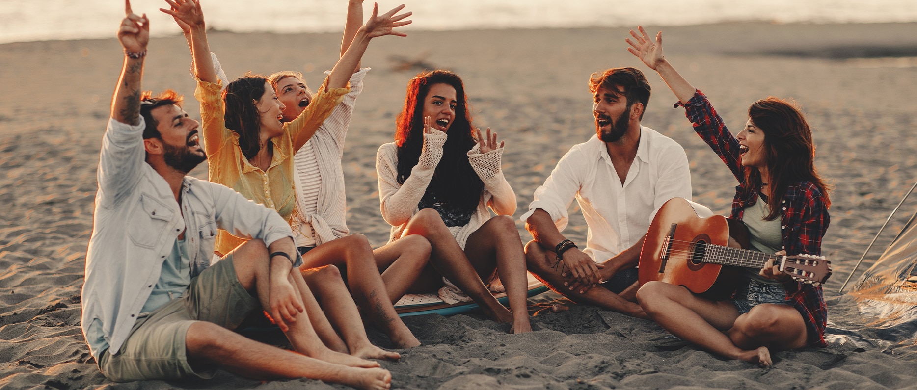 A group of people sitting on a beach together laughing with low sun