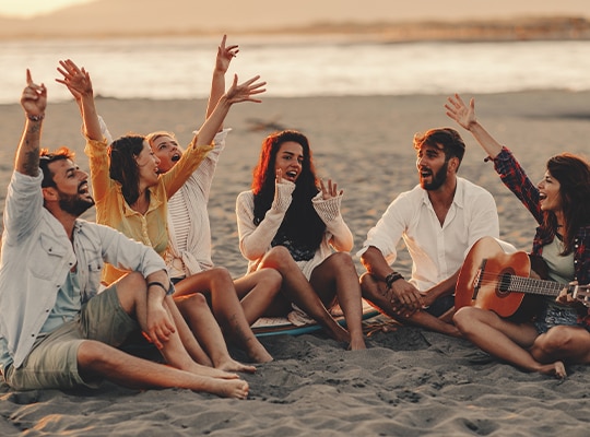 A group of people sitting on a beach together laughing with low sun.