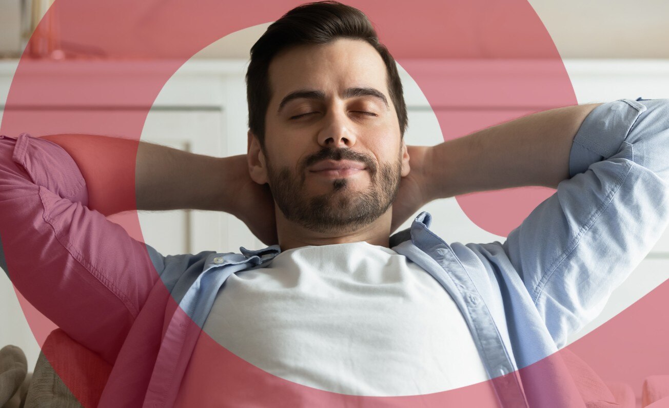 A smiling man with hands behind head relaxing with his eyes closed.